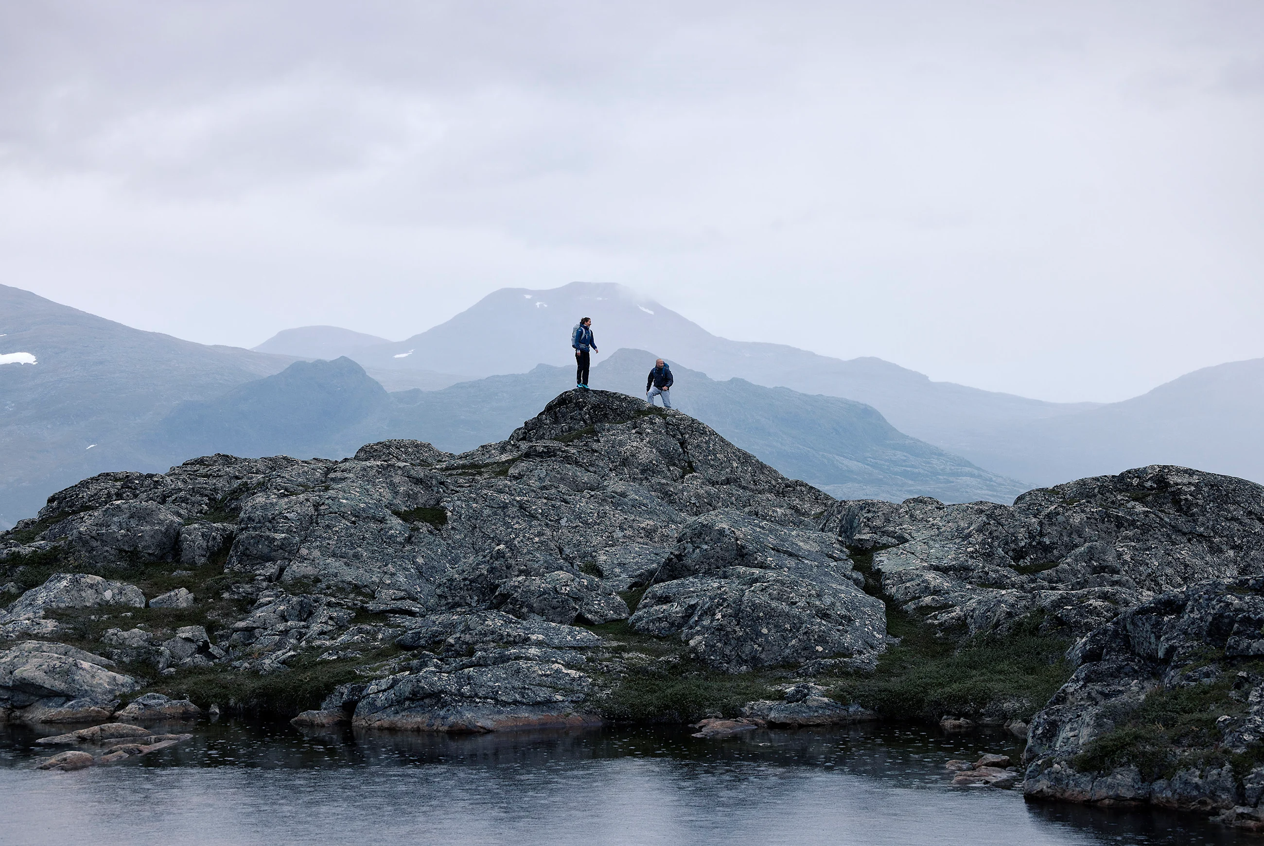 Two hikers on a top beside a lake