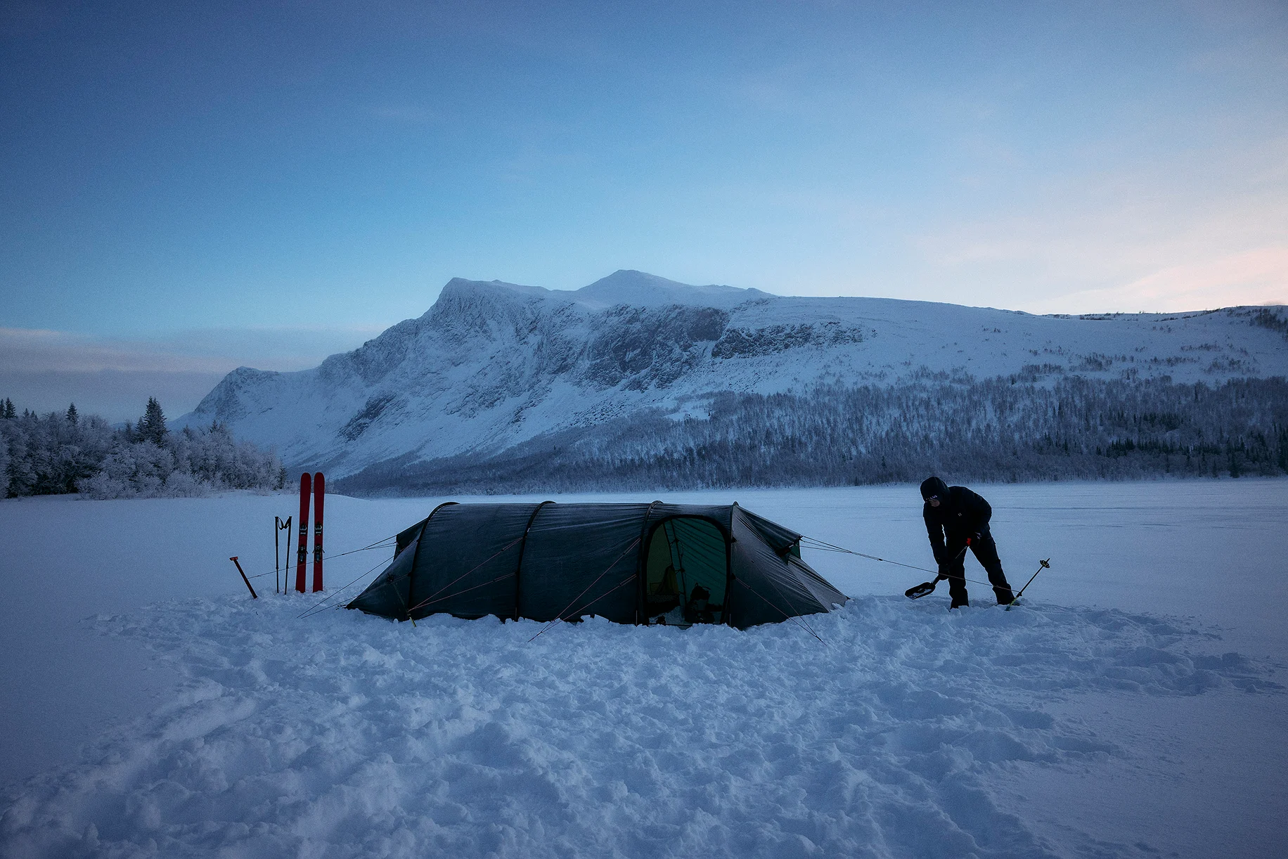 A man stands outside his tent in a snow-covered landscape.
