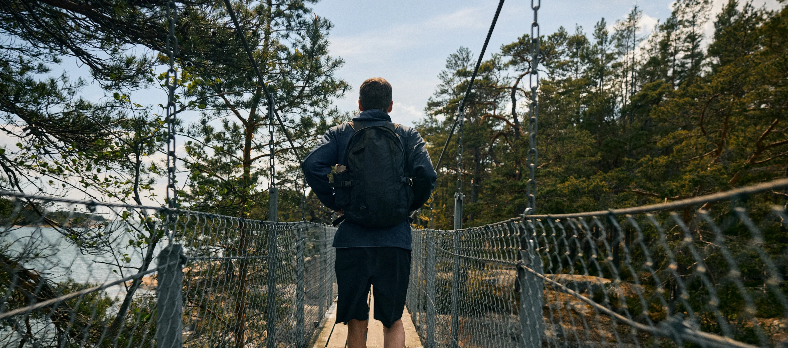 Man with Haglöfs backpack and clothes hiking over a bridge in the summer