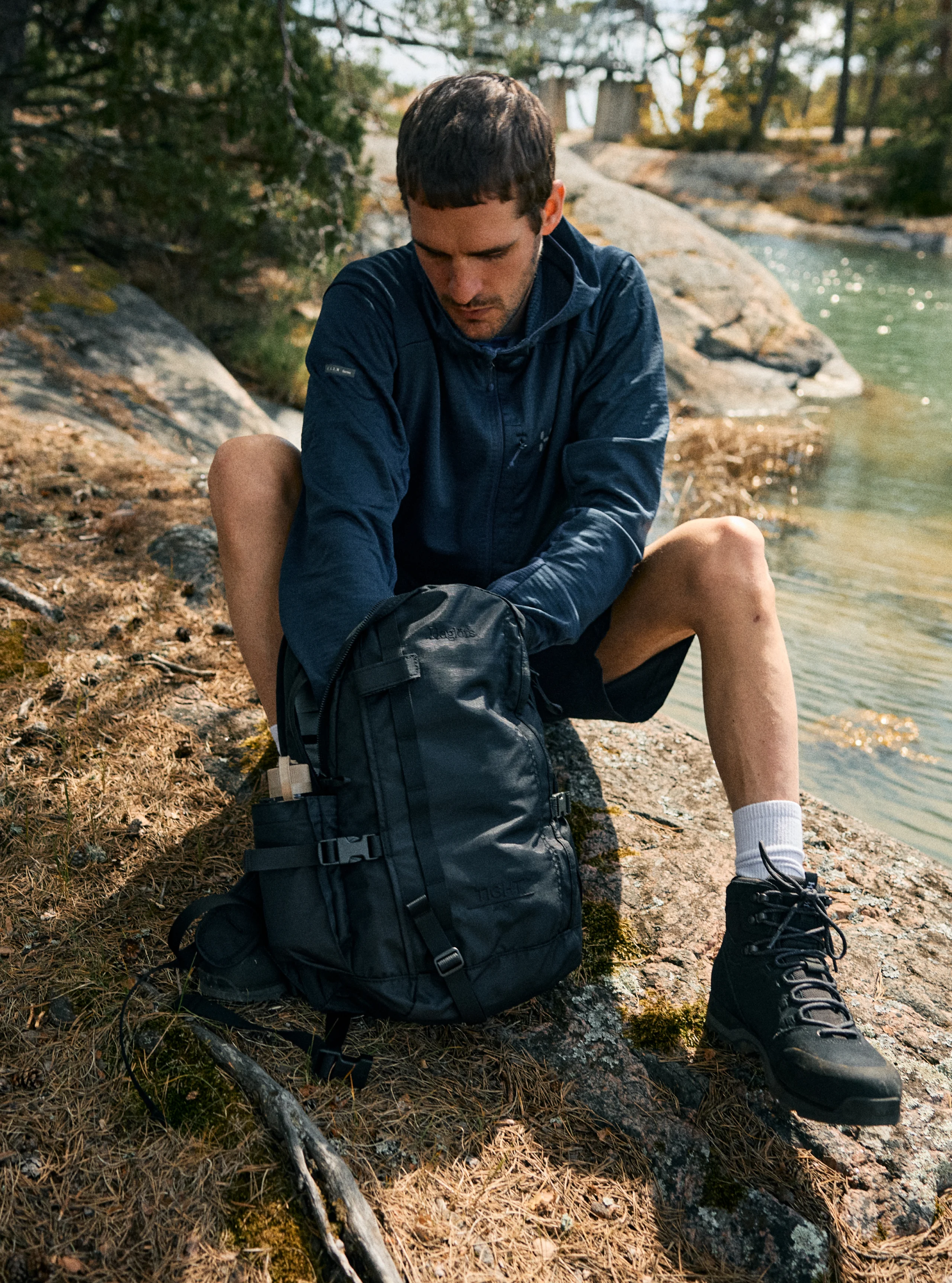 Man sitting in Haglöfs clothes and a tight backpack close to the water during a summer hike