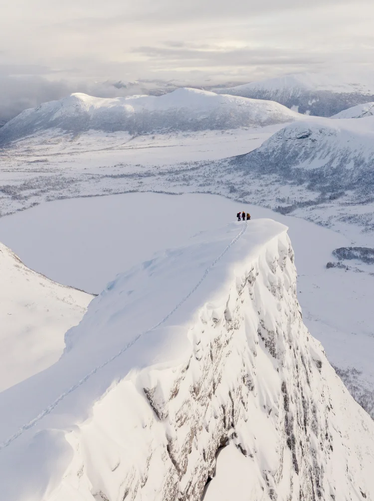 People standing at the end of a large mountain in a winter landscape