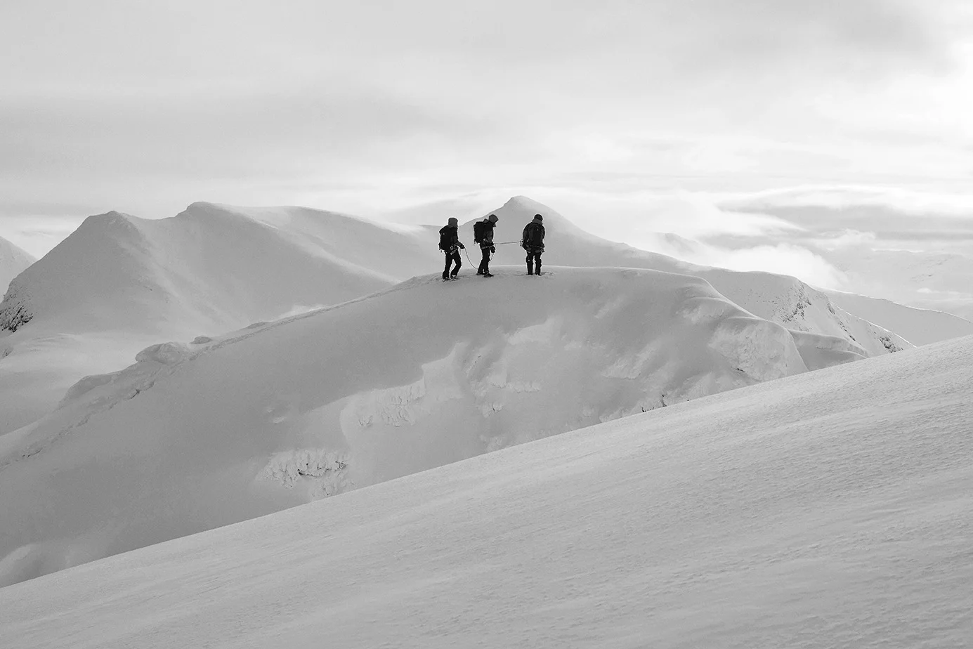 Three people on a snow-covered mountain peak.