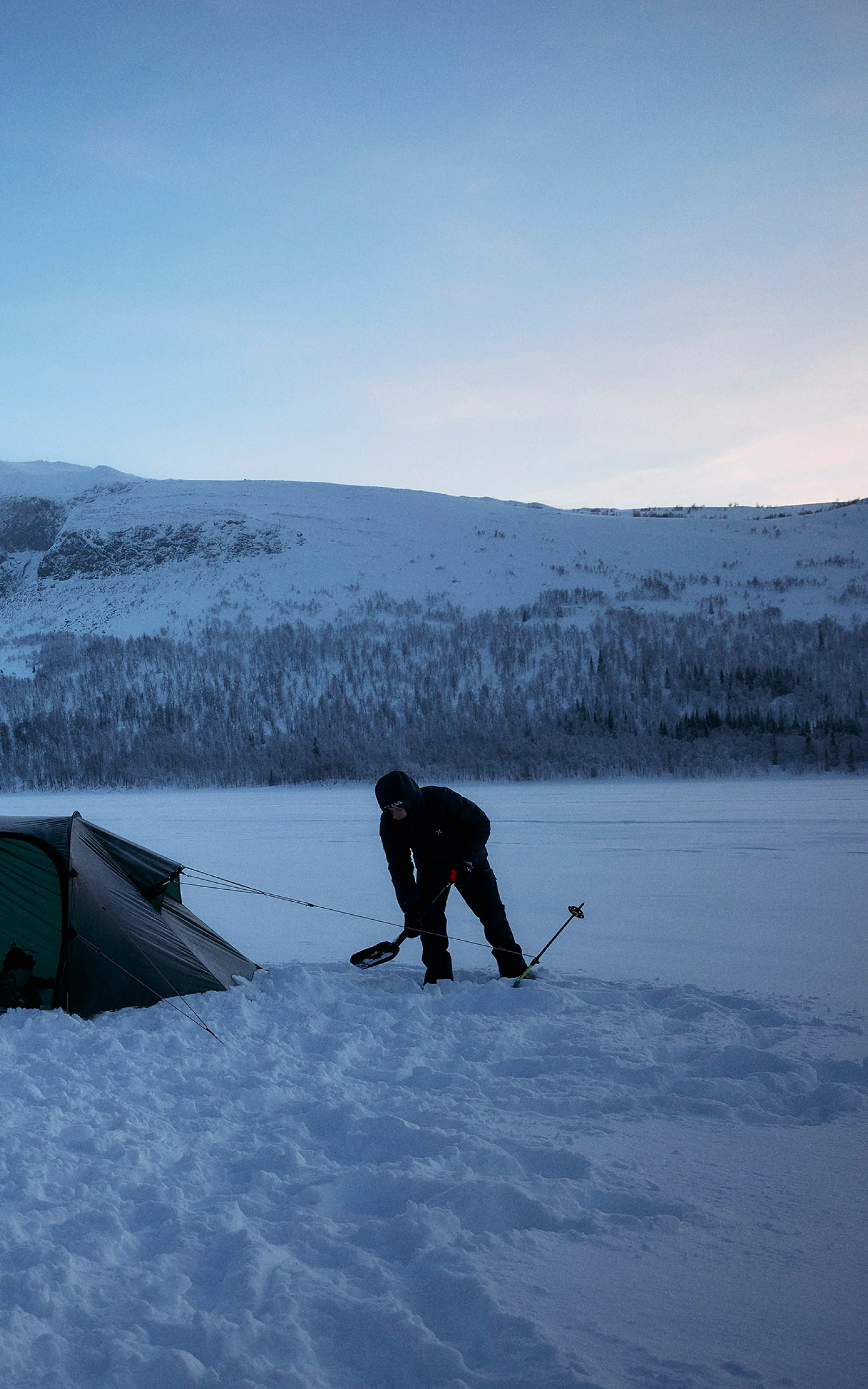 Shoveling snow to protect a tent  in the cold wearing a Haglöfs insulated jacket.