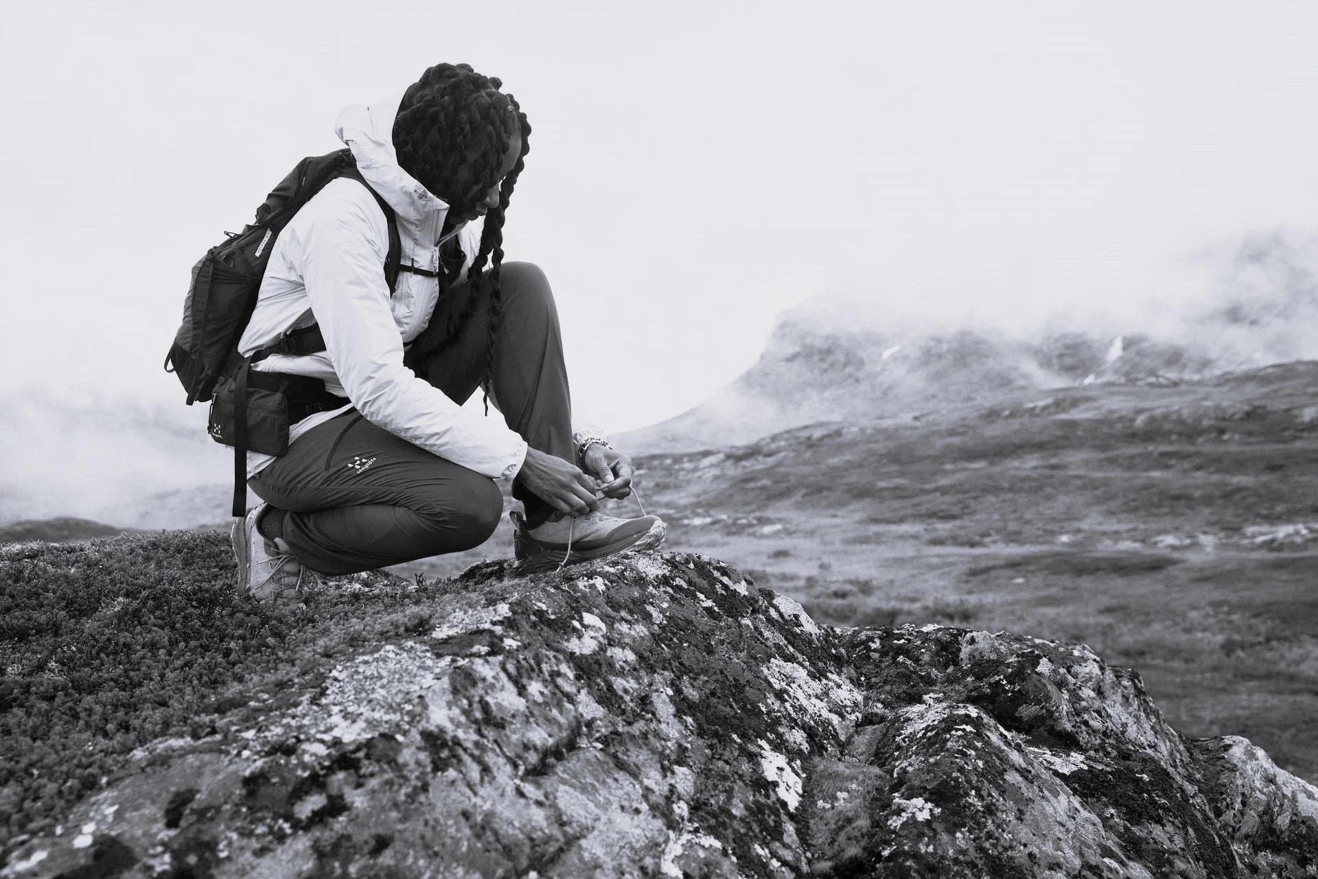 A woman ties her shoes on a mountain.